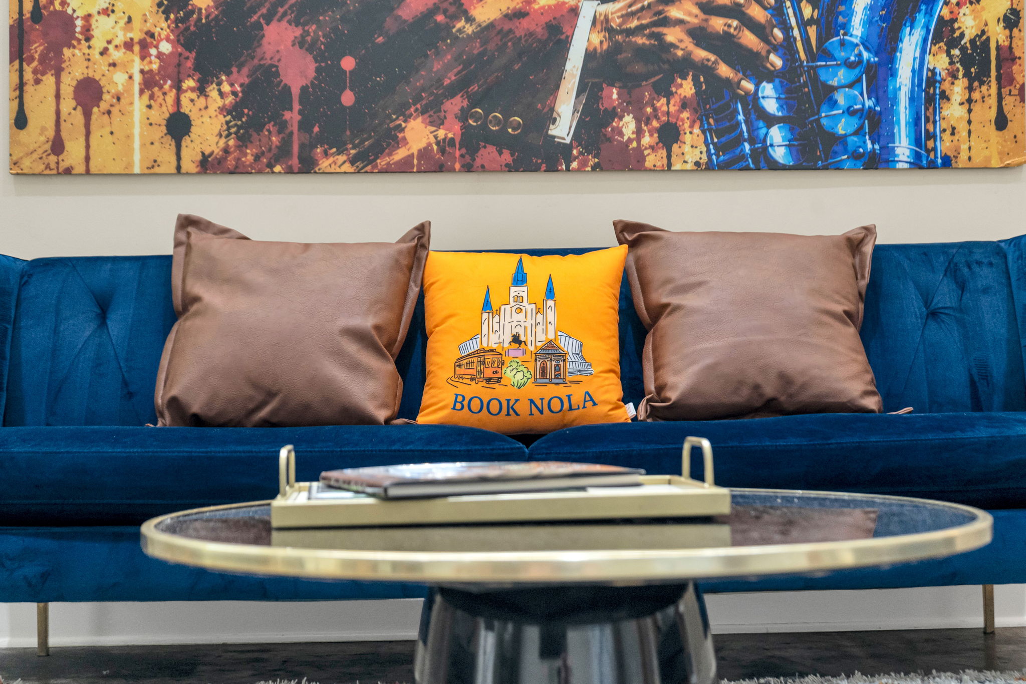 Close-up of the blue velvet sofa with the orange Book NOLA pillow beneath the mural in The Reed suite
