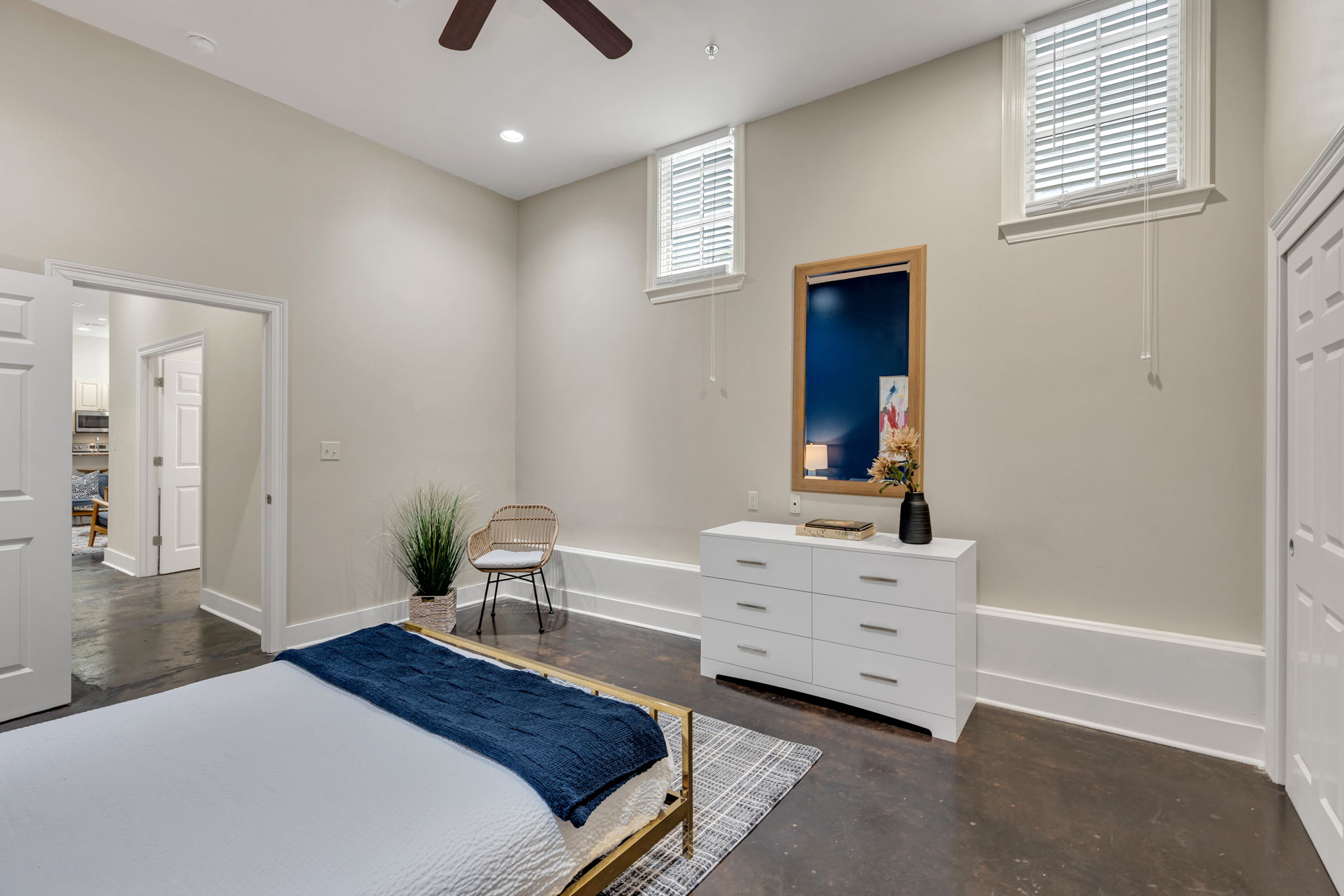 Bedroom with a brass bed frame, navy throw, and white dresser with mirror in The Reed suite