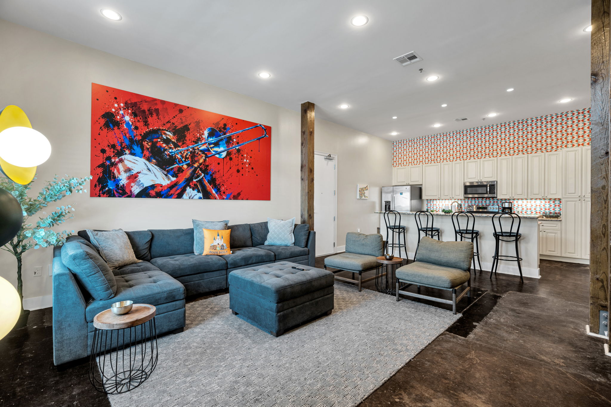 A wide view across the living room in The Slide suite — the mural, the sectional, and the kitchen with its patterned tile backsplash beyond