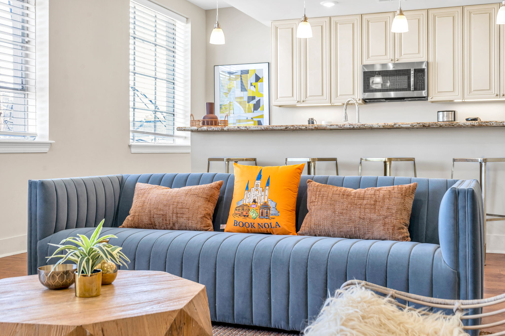 Close-up of the blue channel-tufted sofa with the orange Book NOLA pillow and the kitchen bar behind in The Bell suite