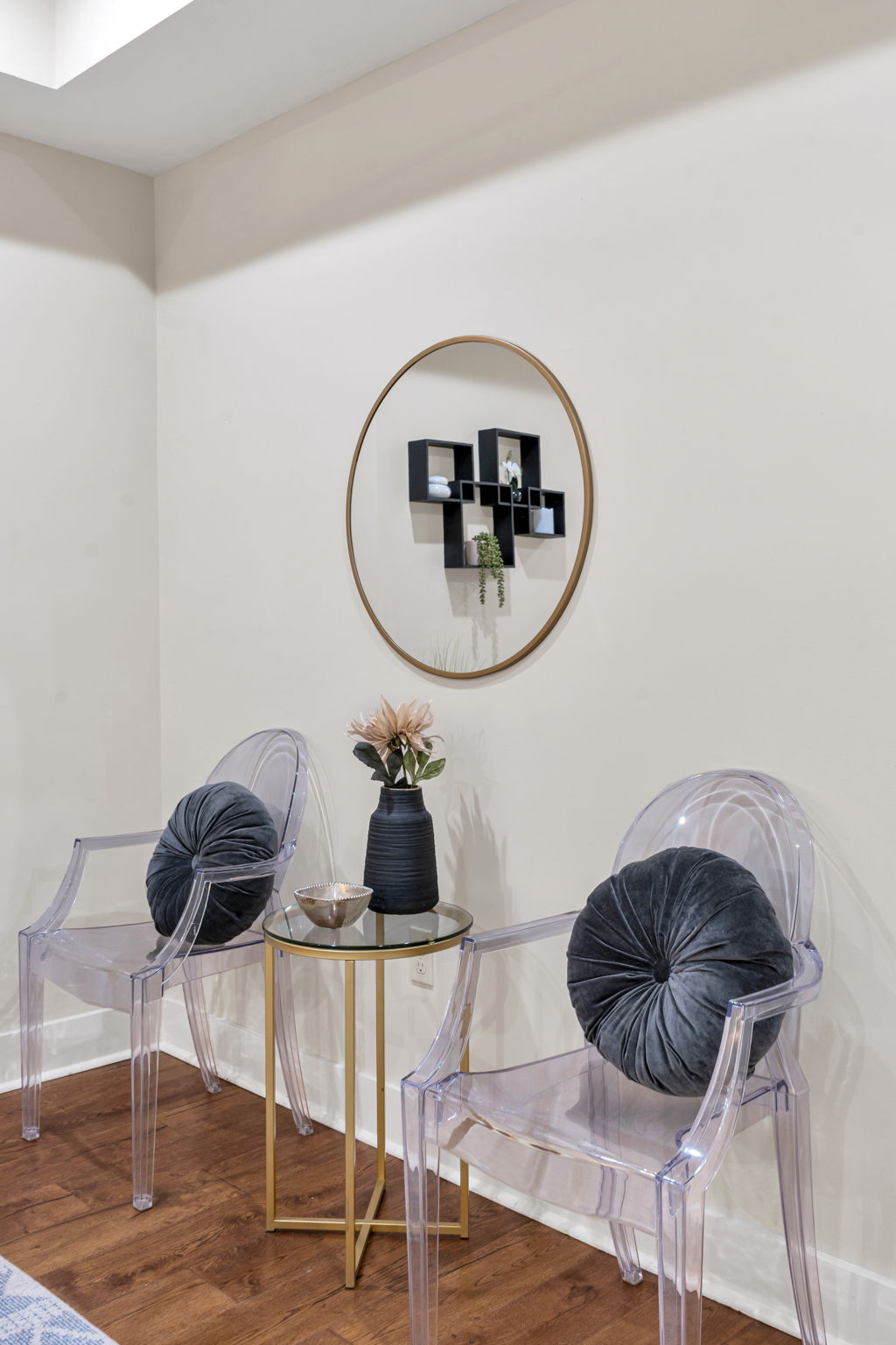 Two clear acrylic ghost chairs with a round mirror and gold side table in The Bell suite