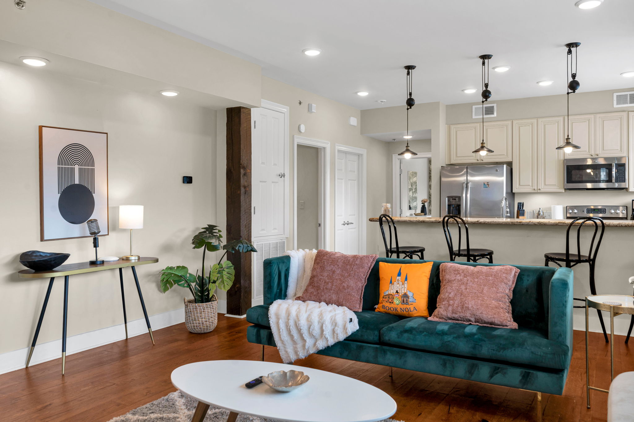 The teal-green velvet sofa with the BOOK NOLA pillow in The Soul suite living room, the vintage-microphone console to the left and the kitchen beyond