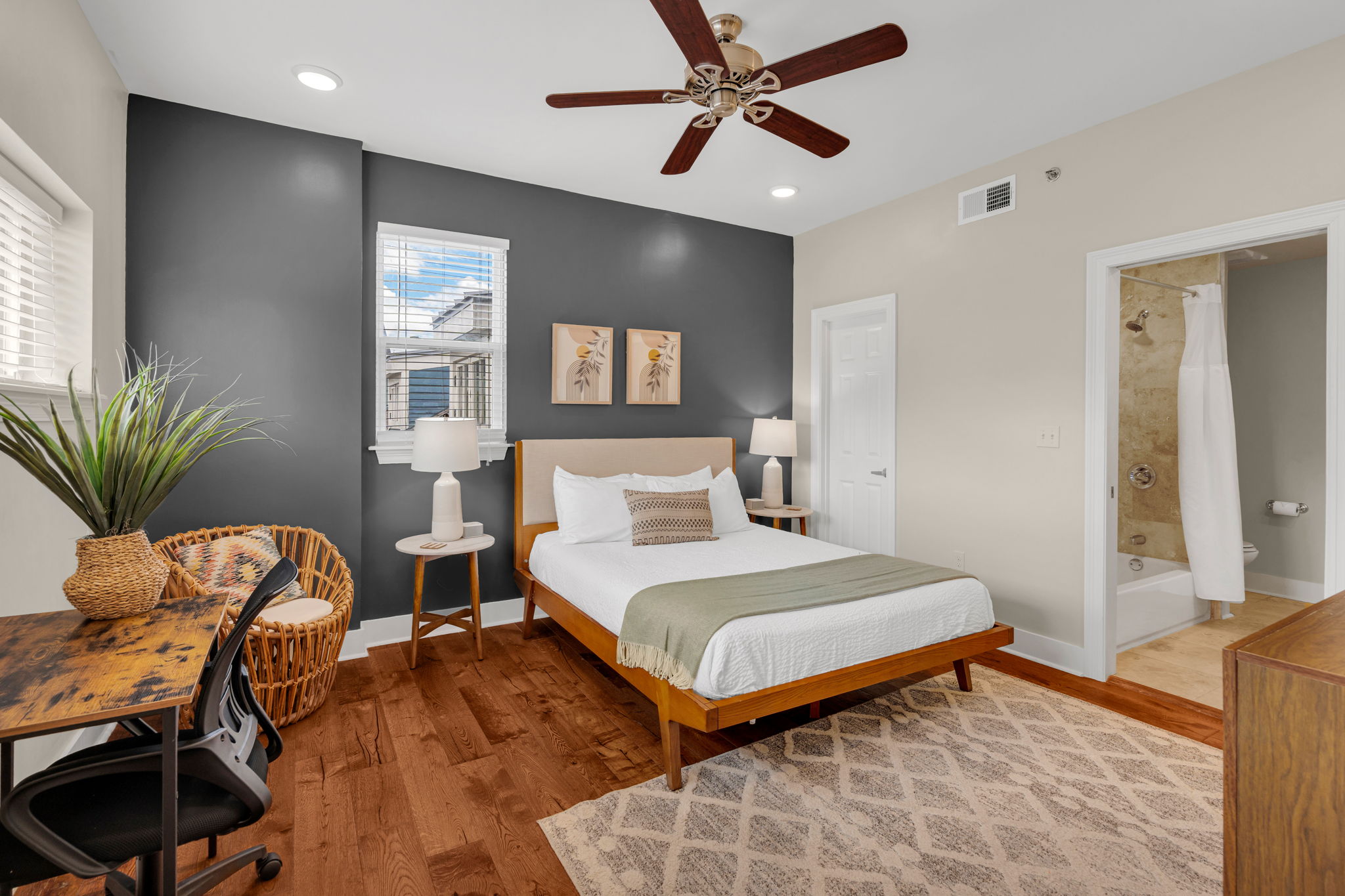 The gray-wall bedroom with the wood bed frame, ceiling fan, desk and wicker chair, and the en-suite bath in The Soul suite