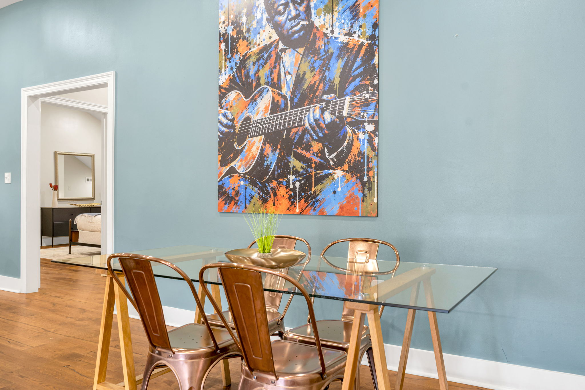 The dining area in The Delta suite — glass table and copper chairs beneath the mural, bedroom doorway at left