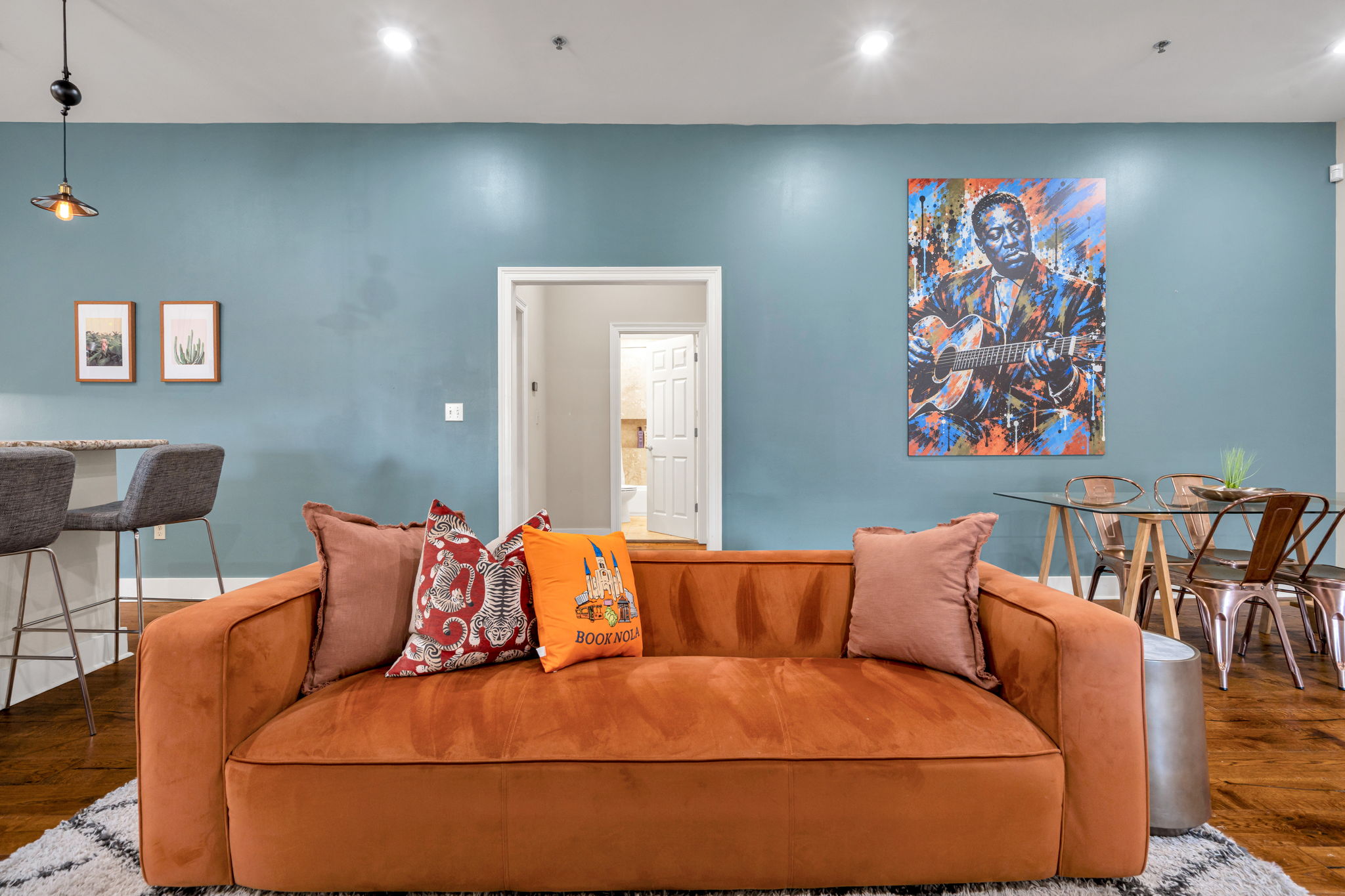 The rust-orange velvet sofa in The Delta suite, head on, with the Book NOLA pillow and the mural on the blue wall behind
