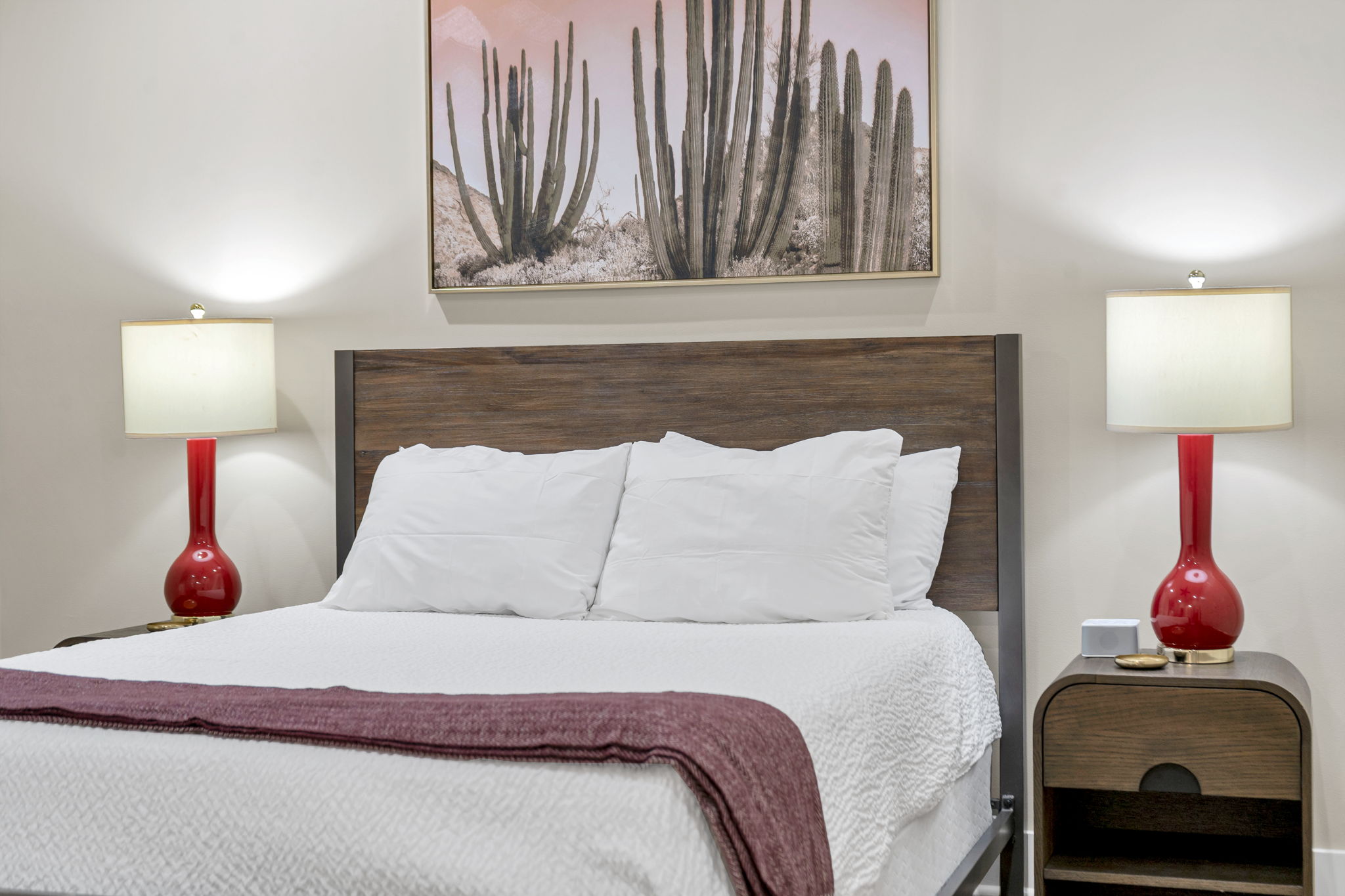 A bedroom in The Delta suite — dark wood headboard, red lamps, and cactus artwork