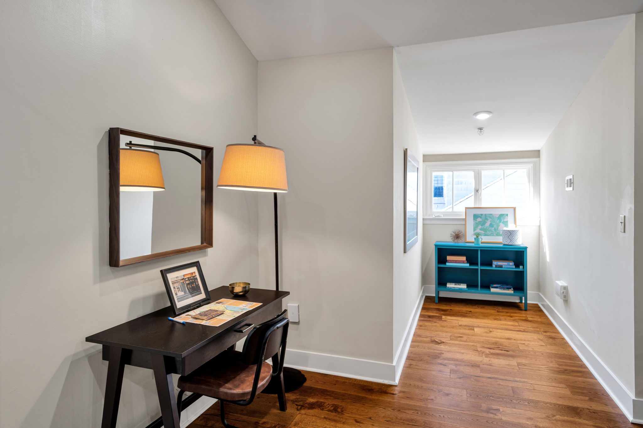 The dark-wood desk with mirror and arc lamp in The Delta suite, looking down the hall to the teal bookcase